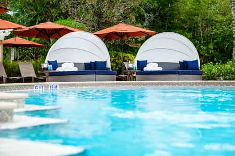 Resort pool with dome-shaped lounge beds, orange umbrellas, and lush green surroundings