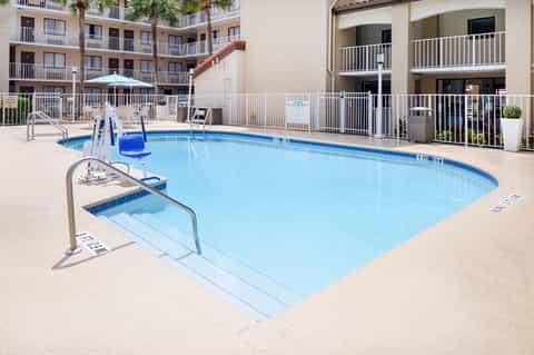 Small rectangular pool with safety railings, slide, lounge chairs, and multi-story residential building behind