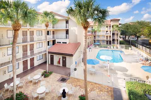 Aerial view of resort courtyard with pool, palm trees, and multi-story beige buildings