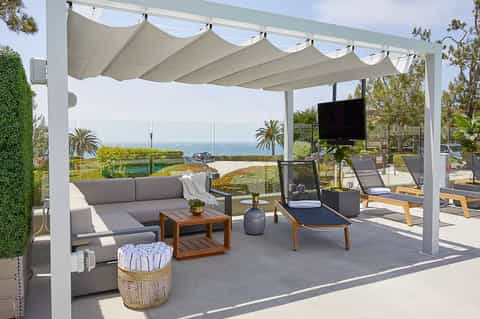 Luxury poolside lounge with white pergola, gray seating, ocean views, and modern landscaping