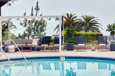 Upscale pool area with modern lounge seating, pergola shade structure, and palm trees