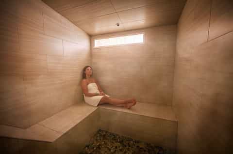 Woman relaxing in wooden sauna with white towel and small window for natural light