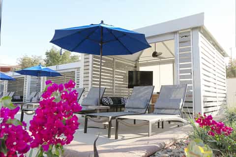 Modern poolside cabanas with blue umbrellas, lounge chairs, and pink flowering plants