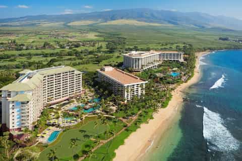 Aerial view of beachfront resort with multiple towers, pools, and mountain backdrop