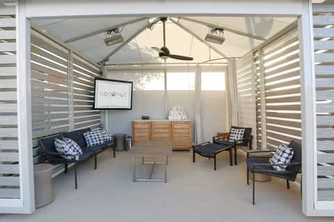 Modern spa relaxation room with white louvered walls, dark seating, and ceiling fan