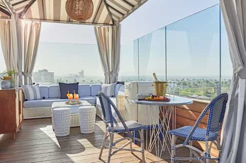 Luxury rooftop lounge with blue seating, striped awning, city skyline views, and champagne
