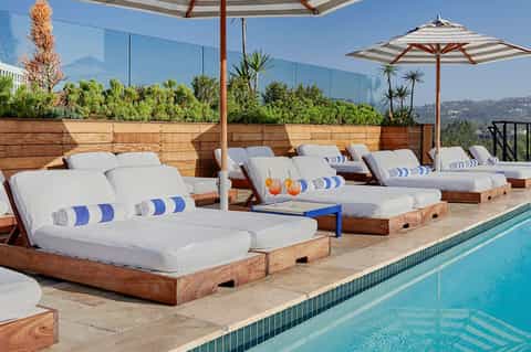 Upscale poolside lounge area with wooden daybeds, striped umbrellas, and mountain views