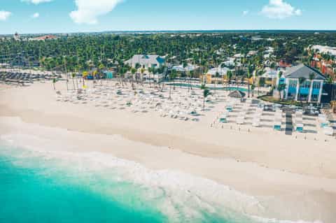 Aerial view of beachfront resort with children's play area, beach umbrellas, and tropical vegetation