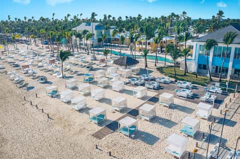 Aerial beach view with white cabanas, loungers, palm trees, and turquoise ocean