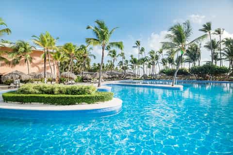 Resort pool surrounded by palm trees, tiki huts, and tropical landscaping