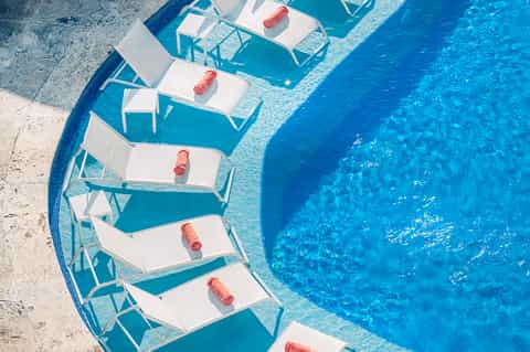 Overhead view of swimming pool with white lounge chairs and rolled towels