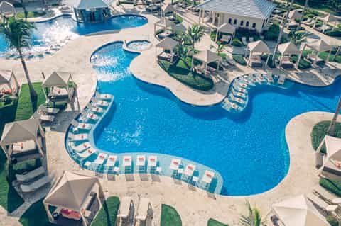 Aerial view of curved resort pool complex with lounge chairs and palm landscaping