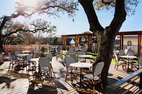 Outdoor terrace with chevron-patterned chairs and tables under a large shade tree