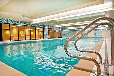 Indoor lap pool with turquoise water, tiled walls, and metal handrails