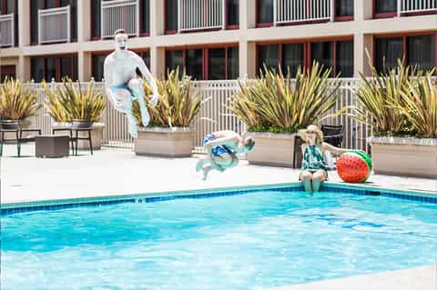 Children playing by pool with animated characters jumping and child in hat sitting poolside