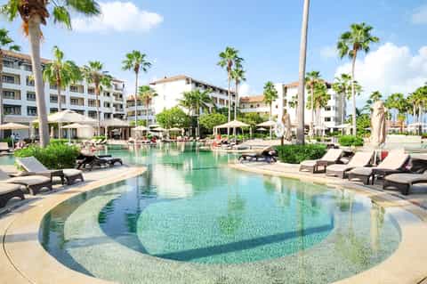 Lagoon-style resort pool with turquoise water, palm trees, loungers, and multi-story buildings