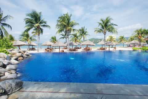 Resort infinity pool with tiki umbrellas overlooking tropical coastline