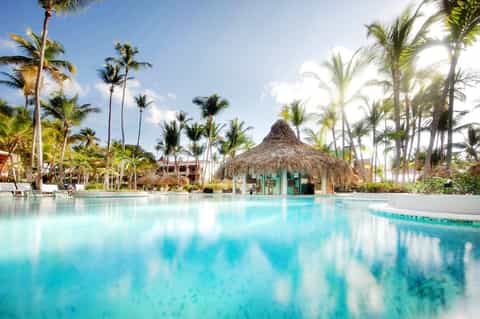 Expansive resort infinity pool with thatched-roof bar, palm trees, and colorful casita-style buildings