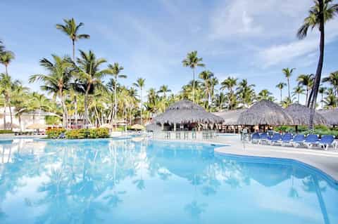 Large lagoon-style pool with palm trees, tiki bars, and lounge chairs at tropical resort