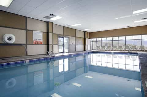 Indoor heated swimming pool with large windows, lounge chairs, and mountain views