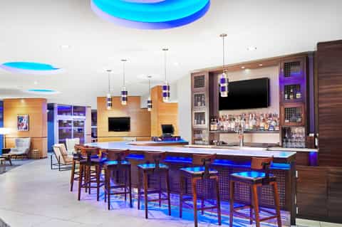 Modern hotel game lounge with pool tables, bar counter, blue accent lighting, and entertainment area