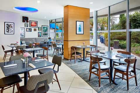 Modern hotel café with mid-century furniture, artwork wall, and glass patio doors