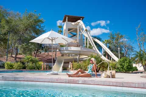 Resort waterslide and pool area with white umbrella, lounging guest, and tropical landscaping
