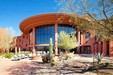 Red-brick resort building with curved glass facade, courtyard with cacti and desert landscaping
