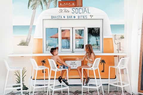 Two children at St. Pete Social beachfront cafe with orange and white striped counter and palm tree
