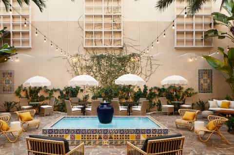 Courtyard pool area with white umbrellas, woven lounge chairs, ivy-covered walls, and string lights overhead
