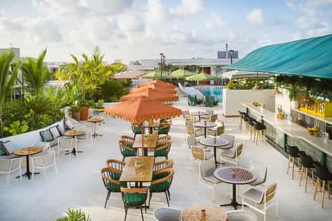 Rooftop terrace with dining tables, orange umbrellas, pool, and tropical plants