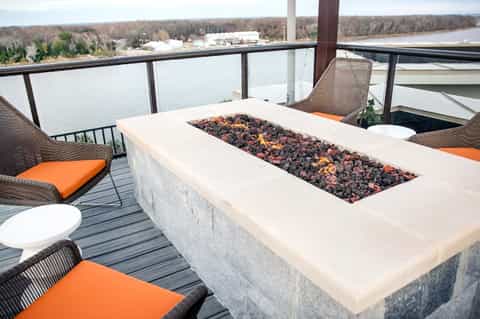 Fire pit table with orange cushioned seating on waterfront deck overlooking scenic river landscape