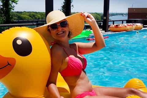Woman in pink bikini relaxing on yellow duck float in resort pool with water toys