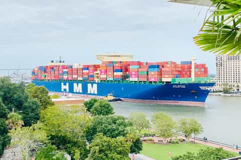 Massive cargo ship laden with colorful containers passing through inland waterway surrounded by greenery