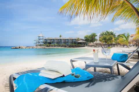 Beach lounge setting with cocktail, book, and towel overlooking tropical waters