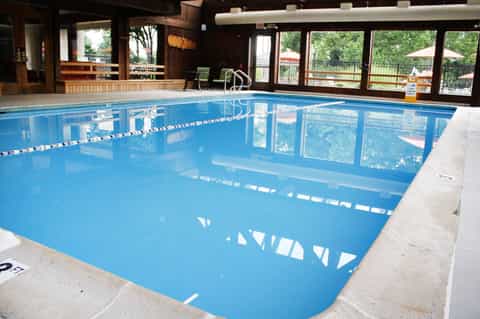 Indoor swimming pool with lane dividers in a wood-paneled facility with large windows overlooking outdoor grounds