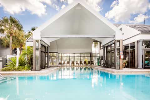 Indoor pool with glass ceiling, white architectural structure, and palm trees