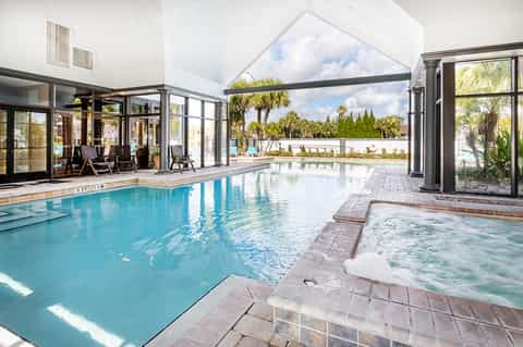 Indoor heated pool with spa, glass doors, and resort views of tropical landscape