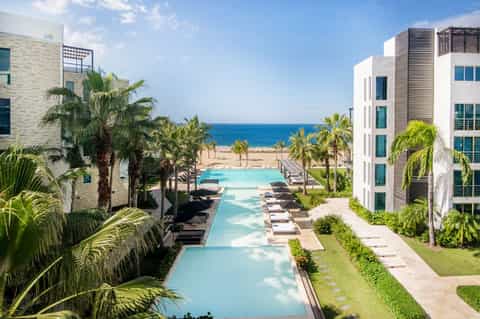 Resort courtyard with turquoise pool, palm trees, and modern white multi-story buildings