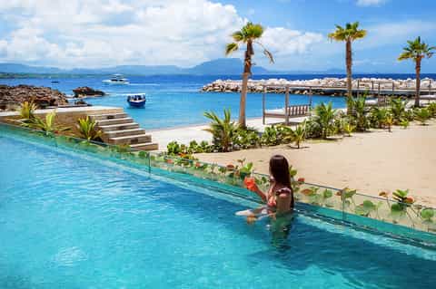 Infinity pool overlooking tropical beach with palm trees and crystal-clear turquoise water