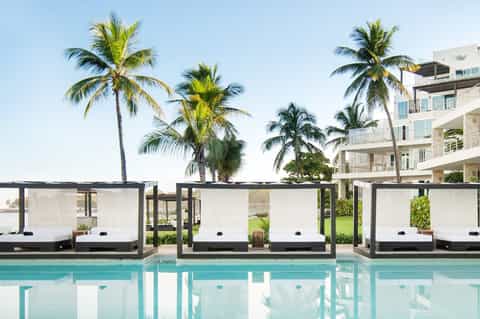 Pool deck with modern white cabanas, palm trees, and residential building backdrop
