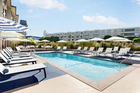 Contemporary pool deck with blue and white striped loungers, umbrellas, modern hotel building, and landscaping