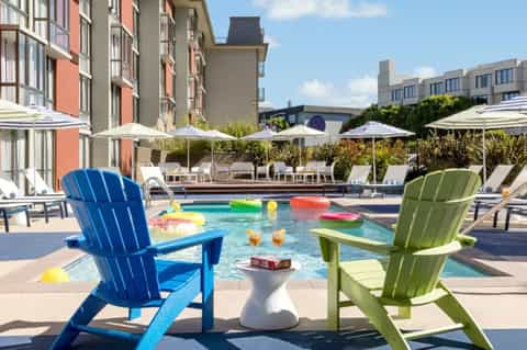 Urban resort pool area with blue and green Adirondack chairs, colorful floats, umbrella shade coverage