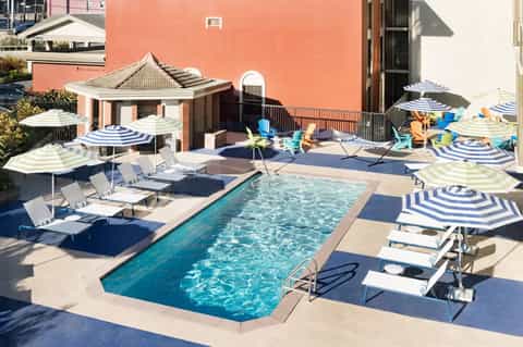 Resort pool deck with striped umbrellas, lounge chairs, coral building, and gazebo on sunny day
