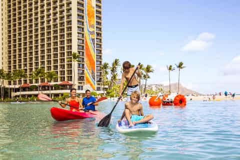 Beachfront resort tower with water sports activities including paddleboards and kayaks in shallow turquoise water