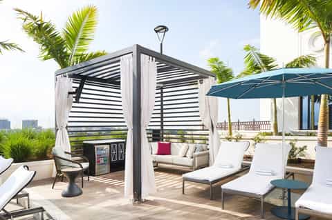 Contemporary resort deck with pergola cabana, loungers, palm trees, and waterfront views