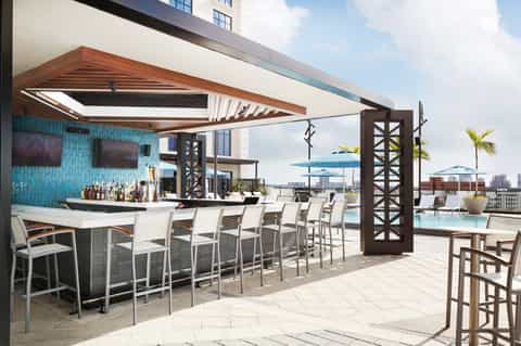 Upscale rooftop bar with turquoise tile, wooden shade structure, and city skyline