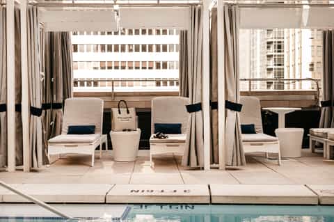 Upscale poolside cabanas with cream curtains and cushioned lounge chairs overlooking water