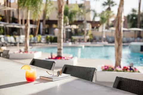 Poolside dining area with cocktail, lounge chairs, and tropical palm trees in background