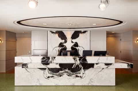 Modern hotel reception desk with white marble and black veining under elliptical ceiling